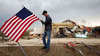 Seorang warga memegang bendera AS di depan puing bangunan akibat tornado di Mayflower, Arkansas, Selasa (29/4/2014). [Reuters/Carlo Allegri]