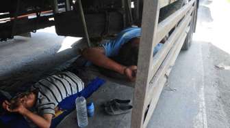 Awak truk tertidur di bawah truknya di jalur pantura Akibat dua jembatan pantura di Comal amblas, Sabtu (19/7). [Antara/Oky Lukmansyah]
