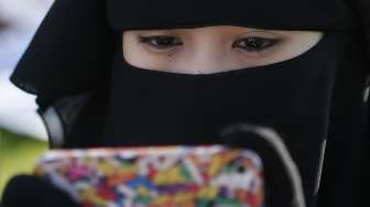 Seorang perempuan Filipina melihat ponselnya selagi menunggu pelaksanaan sholat Idul Fitri di Manila, Filipina, (28/7). (Reuters/Erik De Castro)