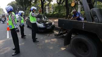 Petugas Polantas menertibkan kendaraan roda empat yang terparkir liar di sepanjang jalan Medan Merdeka Barat Jakarta, Senin (18/8). [suara.com/Kurniawan Mas'ud]