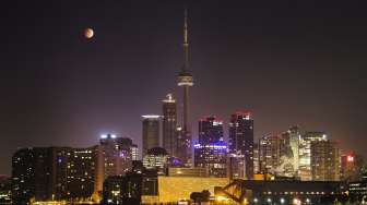 Bulan berubah warna menjadi kemerahan saat gerhana bulan total yang tampak di belakang CN Tower, Toronto, Kanada. (Reuters/Mark Blinch)