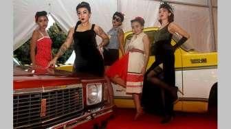 Beberapa orang perempuan bertato berpose di antara jejeran mobil-mobil klasik hot rod yang dipajang di lokasi acara Indonesia Greaser Party 2015, Jumat (10/4/2015), di Plaza Barat Senayan. [Suara.com/Oke Atmaja]