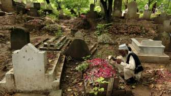 Seorang lelaki Muslim membaca doa di depan kuburan keluarganya di sebuah pemakaman, di hari pertama Idul Fitri, di Rawalpindi, Pakistan, Sabtu (18/7/2015). [Reuters/Faisal Mahmood]