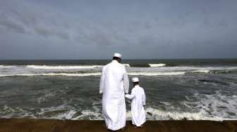 Seorang lelaki warga Muslim Sri Lanka bersama putranya, tampak berdiri di pantai, di pagi hari jelang salat Idul Fitri, di Kolombo, Sabtu (18/7/2015). [Reuters/Dinuka Liyanawatte]