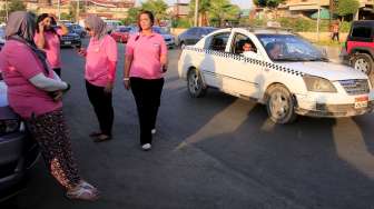 Para sopir perempuan Pink Taxi tampak berdiri di parkiran, sementara sebuah taksi reguler terlihat melintas di dekatnya, di Kairo, Mesir, Minggu (6/9/2015). [Reuters/Amr Abdallah Dalsh]