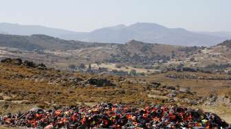 Sejumlah warga Pulau Lesbos, Yunani, melihat tumpukan perahu karet, ban dalam, dan rompi penyelamat yang dipakai oleh para pengungsi dan imigran asal Timur Tengah. [Reuters/Yannis Behrakis]