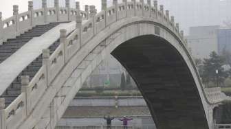 Warga melakukan olah raga di dekat jembatan di hari berkabut di Beijing, Cina, Senin (7/12). [Reuters/Jason Lee]