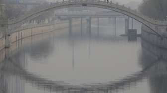 Warga berjalan melintasi jembatan di hari berkabut di Beijing, Cina, Senin (7/12). [Reuters/Jason Lee]