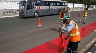 Pekerja melakukan pengecatan jalur bus Transjakarta di flyover Kuningan, Jalan HR Rasuna Said, Kuningan, Jakarta, Minggu (20/12/2015). [Suara.com/Kurniawan Mas'ud]