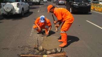 Petugas Penanganan Prasarana dan Sarana Umum (PPSU) menambal jalan berlubang di kawasan Kuningan, Jakarta, Jumat (17/2).