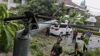 Pohon tumbang yang merobohkan sebuah tiang lampu jalan raya dan menimpa sebuah mobil mewah di Jalan Purworejo, Menteng, Jakarta, Senin (27/11).