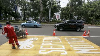 Pekerja mengecat rambu jalur kuning khusus sepeda motor di Jalan Medan Merdeka, Jakarta, Selasa (16/1). 