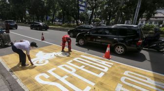 Pekerja mengecat rambu jalur kuning khusus sepeda motor di Jalan Medan Merdeka, Jakarta, Selasa (16/1). 