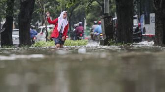 Warga tampak melintas di tengah genangan air banjir di Cempaka Putih, Jakarta, Kamis (15/2/2018). [Suara.com/Kurniawan Mas'ud]