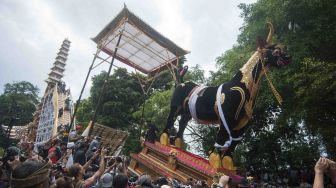 Wisatawan dan warga menyaksikan arak-arakan peti jenazah berbentuk sapi dan keranda bertingkat sembilan atau Bade yang berisi jenazah keluarga Puri (kerajaan) Ubud, Anak Agung Niang Agung dalam upacara Ngaben akbar di Desa Peliatan, Ubud, Bali, Jumat (2/3). 