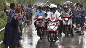 Presiden Joko Widodo berboncengan dengan Ibu Negara Iriana Joko Widodo mengendarai motor listrik menembus hujan saat kunjungan kerja di Distrik Agats, Kabupaten Asmat, Papua, Kamis (12/4).