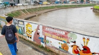 Warga melintas di depan mural ajakan menjaga kebersihan di dinding turap Kali Ciliwung, Kampung Melayu, Jatinegara, Jakarta, Jumat (27/4). 