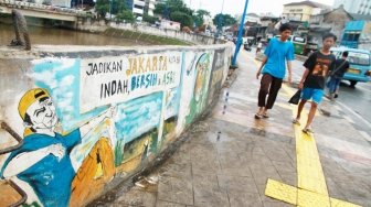 Warga melintas di depan mural ajakan menjaga kebersihan di dinding turap Kali Ciliwung, Kampung Melayu, Jatinegara, Jakarta, Jumat (27/4). 