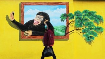 Sejumlah warga tampak melintas di samping beberapa lukisan mural tiga dimensi di kawasan Jatinegara, Jakarta, Jumat (6/7/2018). [Suara.com/Muhaimin A Untung]