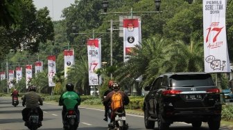 Sejumlah pengendara terlihat melintas di samping spanduk sosialisasi Pemilu Serentak 2019 KPU di kawasan Jalan Imam Bonjol, Jakarta, Selasa (10/7/2018). [Suara.com/Oke Atmaja]