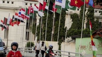 Warga melintas dan beraktivitas di samping deretan bendera negara peserta Asian Games 2018 yang dipasang di kawasan Kali Besar, Kota Tua, Jakarta, Jumat (20/7/2018). [Suara.com/Muhaimin A Untung]