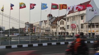 Warga melintas dan beraktivitas di samping deretan bendera negara peserta Asian Games 2018 yang dipasang di kawasan Kali Besar, Kota Tua, Jakarta, Jumat (20/7/2018). [Suara.com/Muhaimin A Untung]