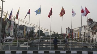 Warga melintas dan beraktivitas di samping deretan bendera negara peserta Asian Games 2018 yang dipasang di kawasan Kali Besar, Kota Tua, Jakarta, Jumat (20/7/2018). [Suara.com/Muhaimin A Untung]