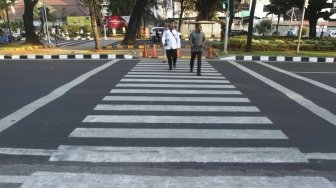 Warga menyebrang melalui Pelican Crosing di kawasan Merdeka Barat, Jakarta, Sabtu (28/7). Pemprov DKI Jakarta segera membuat pelican crossing sebagai pengganti jembatan penyeberangan orang (JPO) di Bundaran HI yang akan dirobohkan dengan alasan keindahan dan tak ramah difabel. [suara.com/Muhaimin A Untung]