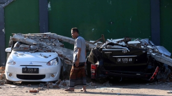 Warga melintas di antara mobil yang rusak akibat gempa bumi, Tanjung, Lombok Utara, NTB, Senin (6/8). BNPB mencatat sedikitnya 91 orang korban meninggal dunia akibat bencana gempa bumi yang terjadi Minggu (5/8) dan terdapat kemungkinan akan bertambah. ANTARA FOTO/Zabur Karuru