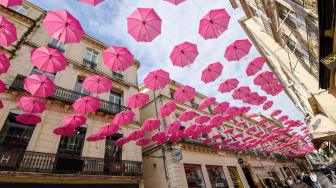 Pejalan kaki melintasi ratusan payung pink yang digantung di Montpellir, Prancis, Selasa (9/10). [AFP/PASCAL GUYOT]
