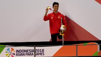 Perenang Indonesia Jendi Pangabean menunjukkan medali emas yang diperolehnya dari nomor renang 100 meter gaya punggung putra S9 Asian Para Games 2018 di Stadion Akuatik, Senayan, Jakarta, Kamis (11/10). [ANTARA FOTO/Akbar Nugroho Gumay]