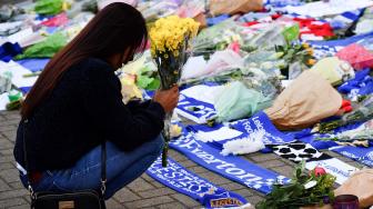 Seorang wanita meletakkan karangan bunga sebagai tanda duka cita di luar Stadion King Power Stadium, Leicester, Inggris, Minggu (28/10). [AFP/Ben STANSALL]