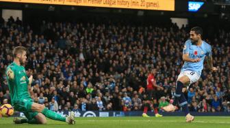 Gelandang Manchester City Ilkay Gundogan menembak dan mencetak gol ketiga usai melewati kiper Manchester United David de Gea selama pertandingan sepak bola Liga Primer Inggris antara Manchester City melawan Manchester United di Etihad Stadium, Manchester, Inggris, Minggu (11/11). [AFP/Lindsey PARNABY]