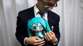 Akihiko Kondo berpose dengan bonek aktris virtual, Hatsume Miku sambil mengenakan cincin kawin di Tokyo, Jepang, Sabtu (10/11). (AFP/Behrouz MEHRI)