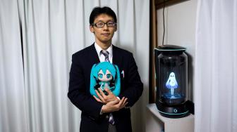 Akihiko Kondo berpose di sebelah hologram yang menampilkan gambar aktris virtual, Hatsune Miku di Tokyo, Jepang, Sabtu (10/11). (AFP/Behrouz MEHRI)