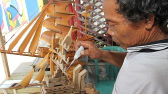 Pengrajin miniatur kapal pinisi menyelesaikan proses pembuatan di Marunda, Jakarta Utara, Selasa (13/11).(Suara.com/Fakhri Hermansyah)