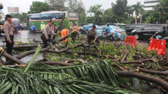 Petugas PPSU (Penanganan Prasarana dan Sarana Umum) bersama anggota Polisi membersihkan batang pohon yang menutupi jalan di daerah Sudirman, Jakarta Pusat, Kamis (22/11). (Suara.com/Fakhri Hermansyah)