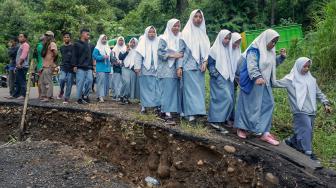 Sejumlah pelajar terpaksa berjalan kaki untuk kemudian berganti kendaraan menuju sekolah saat melewati jalan yang ambles di Desa Tenogo, Paninggaran, Kabupaten Pekalongan, Jawa Tengah, Rabu (23/1). [ANTARA FOTO/Harviyan Perdana Putra]