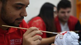 Mahasiswa asing asal Vietnam, Tajikistan dan Kanada menghias patung babi yang terbuat dari tanah liat di Universitas Surabaya, Surabaya, Jawa Timur, Selasa (29/1). ANTARA FOTO/Zabur Karuru