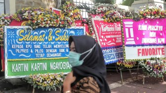 Warga melintas di samping karangan bunga di Kantor KPU, Jakarta, Minggu (21/4). [Suara.com/Muhaimin A Untung]