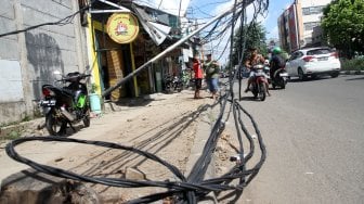 Warga melintasi tiang listrik yang roboh di Jalan Tanjung Duren Raya, Jakarta Barat, (5/2). [Suara.com/Arief Hermawan P]