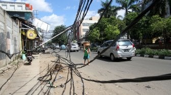 Warga melintasi tiang listrik yang roboh di Jalan Tanjung Duren Raya, Jakarta Barat, (5/2). [Suara.com/Arief Hermawan P]