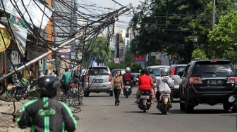 Warga melintasi tiang listrik yang roboh di Jalan Tanjung Duren Raya, Jakarta Barat, (5/2). [Suara.com/Arief Hermawan P]