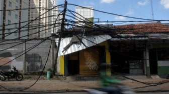 Warga melintasi tiang listrik yang roboh di Jalan Tanjung Duren Raya, Jakarta Barat, (5/2). [Suara.com/Arief Hermawan P]