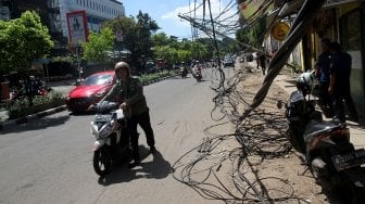 Warga melintasi tiang listrik yang roboh di Jalan Tanjung Duren Raya, Jakarta Barat, (5/2). [Suara.com/Arief Hermawan P]