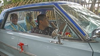 Pasangan pengantin naik mobil antik saat Nikah Bareng di Kampung Mataram, Bantul, DI Yogyakarta, MInggu (12/5). [ANTARA FOTO/Hendra Nurdiyansyah]