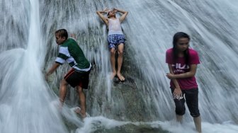 Sejumlah pengunjung menikmati air terjun Bantimurung di objek wisata Bantimurung Maros, Sulawesi Selatan, Jumat (7/6).[Suara.com/Muhaimin A Untung]
