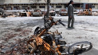 Warga melintas di antara bangkai mobil dan sepeda motor yang hangus terbakar di Kantor Bupati Jayawijaya, Wamena, Papua, Rabu (9/10). [ANTARA FOTO/M Risyal Hidayat]