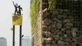 Aktivis Greenpeace membentangkan spanduk di Patung Selamat Datang, di Bundaran HI, Jakarta, Rabu (23/10).[Suara.com/Arya Manggala]