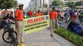 Petugas Satpol PP membentangkan spanduk larangan berjualan di jalur Hari Bebas Kendaraan Bermotor atau Car Free Day, Bundaran HI, Jakarta, Minggu (3/11). [Suara.com/Arya Manggala]